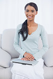 Cheerful attractive woman sitting on cosy sofa with her laptop on her laps