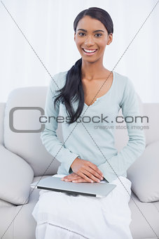 Cheerful attractive woman sitting on cosy sofa with her laptop on her laps