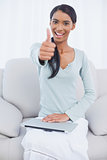Cheerful attractive woman sitting on cosy sofa giving thumbs up