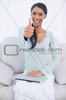Cheerful attractive woman sitting on cosy sofa giving thumbs up