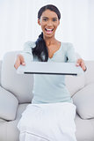 Cheerful attractive woman sitting on cosy sofa holding her laptop