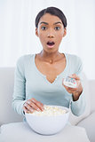 Surprised attractive woman eating popcorn while watching tv