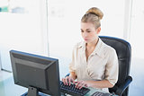Stern young blonde businesswoman looking at her computer
