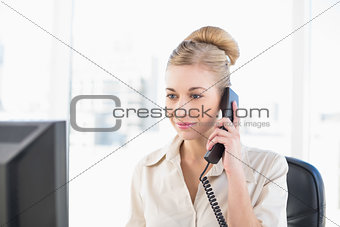 Serious young blonde businesswoman answering the telephone
