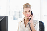 Stern young blonde businesswoman answering the telephone