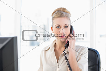 Stern young blonde businesswoman answering the telephone