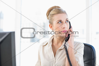 Thoughtful young blonde businesswoman answering the telephone