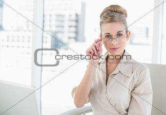 Serious young blonde businesswoman looking over her glasses
