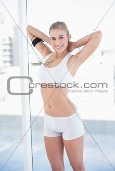 Content young blonde model stretching her arms and listening to music