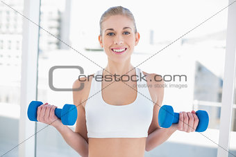 Happy young blonde model exercising with dumbbells