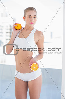Unsmiling young blonde model holding an orange and a half