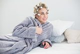 Smiling relaxed blonde woman in hair curlers posing lying on her bed