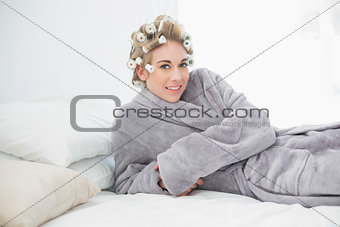 Pleased relaxed blonde woman in hair curlers lying on her bed