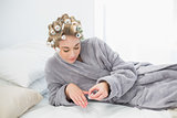 Concentrated relaxed blonde woman in hair curlers applying nail polish