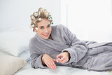 Delighted relaxed blonde woman in hair curlers applying nail polish