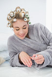 Content relaxed blonde woman in hair curlers applying nail polish