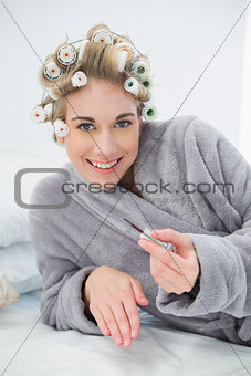 Cheerful relaxed blonde woman in hair curlers applying nail polish