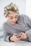 Smiling relaxed blonde woman in hair curlers using her mobile phone