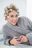 Joyful relaxed blonde woman in hair curlers using her mobile phone