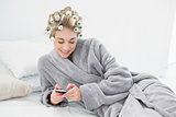 Happy relaxed blonde woman in hair curlers using her mobile phone