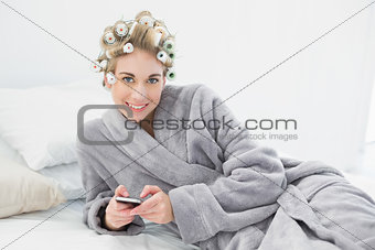 Pleased relaxed blonde woman in hair curlers using her mobile phone