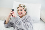 Content relaxed blonde woman in hair curlers looking at her mobile phone