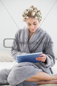 Concentrated relaxed blonde woman in hair curlers using a tablet pc