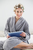 Pleased relaxed blonde woman in hair curlers using a tablet pc