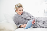 Charming relaxed blonde woman in hair curlers using a tablet pc