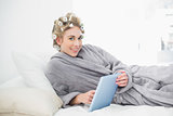Content relaxed blonde woman in hair curlers using a tablet pc