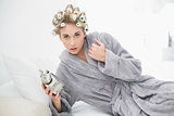 Worried blonde woman in hair curlers holding an alarm clock