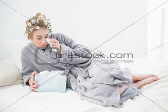 Sad blonde woman in hair curlers crying and using tissues