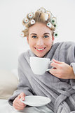 Pleased relaxed blonde woman in hair curlers enjoying a cup of coffee