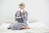 Attractive relaxed blonde woman in hair curlers drinking coffee