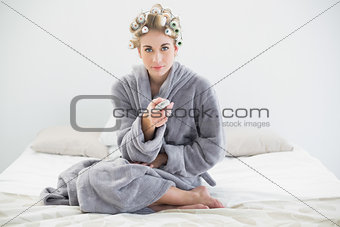 Pretty relaxed blonde woman in hair curlers using remote control