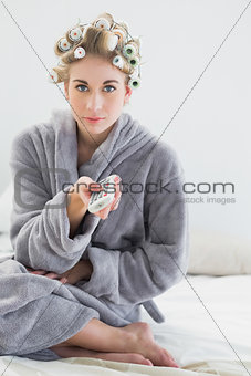 Lovely relaxed blonde woman in hair curlers using a remote control