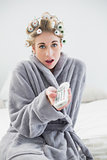 Surprised relaxed blonde woman in hair curlers using a remote control