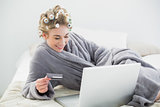 Delighted relaxed blonde woman in hair curlers buying online with her laptop