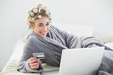 Joyful relaxed blonde woman in hair curlers buying online with her laptop