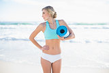 Cute blonde woman in sportswear holding an exercise mat