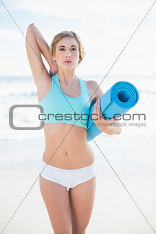 Attractive blonde woman in sportswear carrying an exercise mat