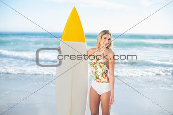 Amused blonde model in swimsuit holding a surfboard