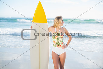 Thoughtful blonde model in swimsuit holding a surfboard