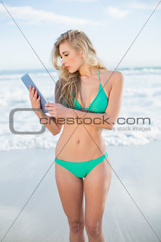 Pensive blonde model in green bikini using a tablet pc
