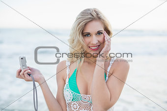 Content blonde woman in white beach dress taking a picture of herself