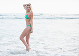 Gorgeous blonde woman in green bikini walking in the waves