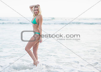 Gorgeous blonde woman in green bikini walking in the waves