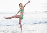 Happy blonde woman in green bikini playing in the waves