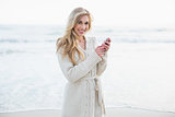Smiling blonde woman in wool cardigan using a mobile phone