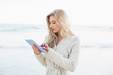 Pensive blonde woman in wool cardigan using a tablet pc